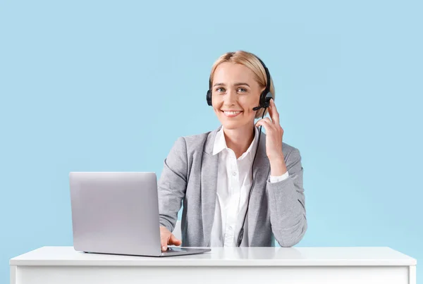 Junge Helpdesk-Betreiberin mit Laptop und Headset sitzt am Tisch vor blauem Hintergrund — Stockfoto