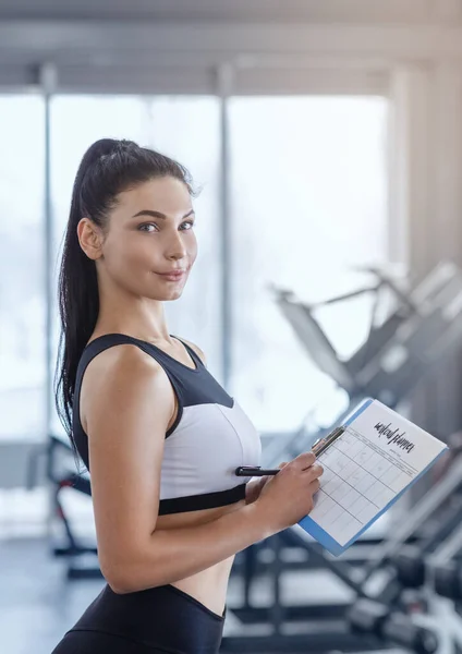 Attractive personal trainer composing workout schedule for client at gym — Stock Photo, Image