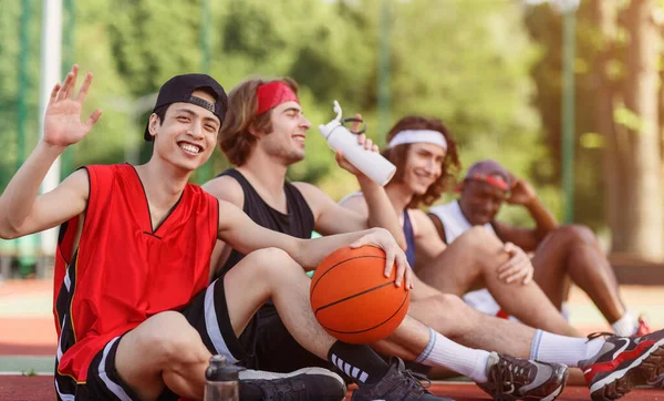 Jugador asiático y su equipo multinacional descansando en la arena de baloncesto al aire libre, espacio vacío — Foto de Stock