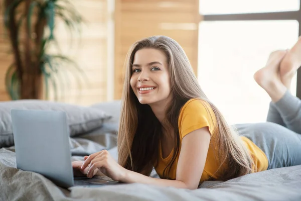 Mujer feliz usando el ordenador portátil mientras está acostado en la cama por la mañana — Foto de Stock