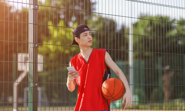 Pemain Asia serius dengan smartphone di arena basket outdoor — Stok Foto
