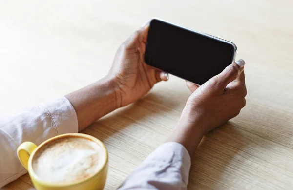 Обрізаний вид молодої жінки, що тримає смартфон з порожнім екраном, п'є каву в кафе, макет для дизайну — стокове фото