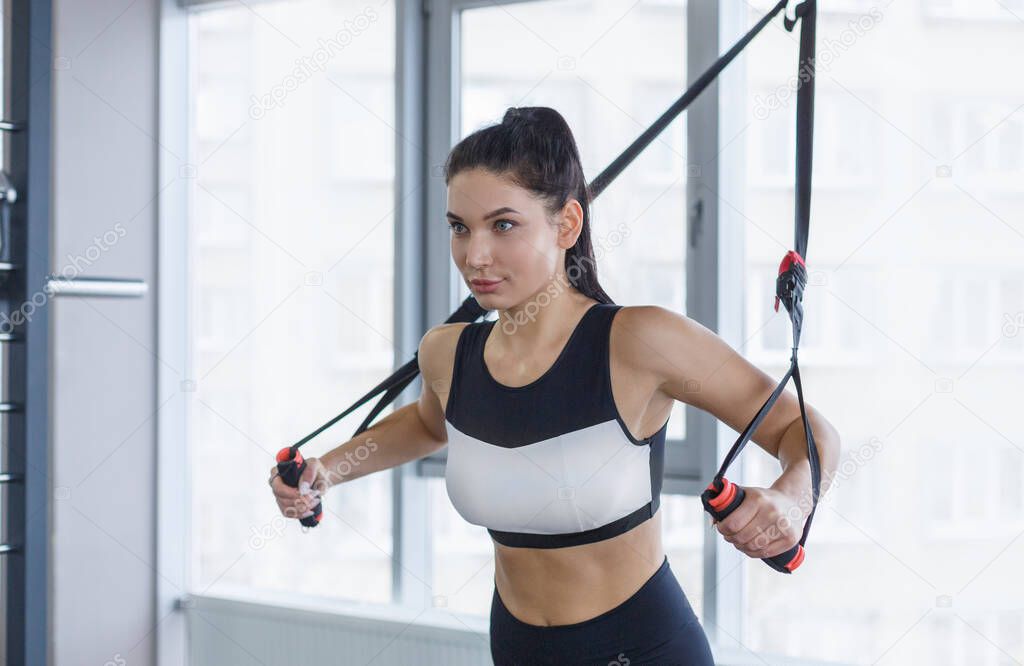 Strong girl working out with cable machine, lifting weights at gym