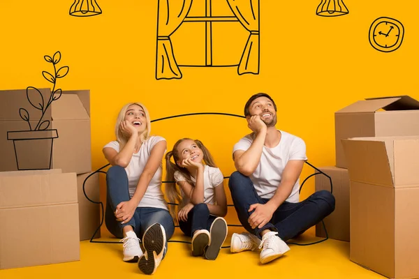 Glada föräldrar och barn med kartonger föreställa sig sitt nya hem på orange bakgrund med ritningar — Stockfoto