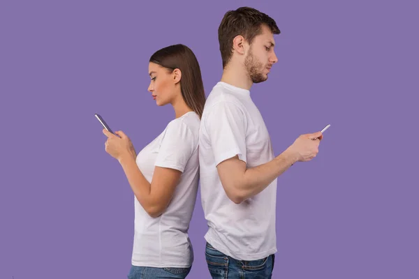 Портрет молодой пары, стоящей спиной к спине с помощью телефонов — стоковое фото