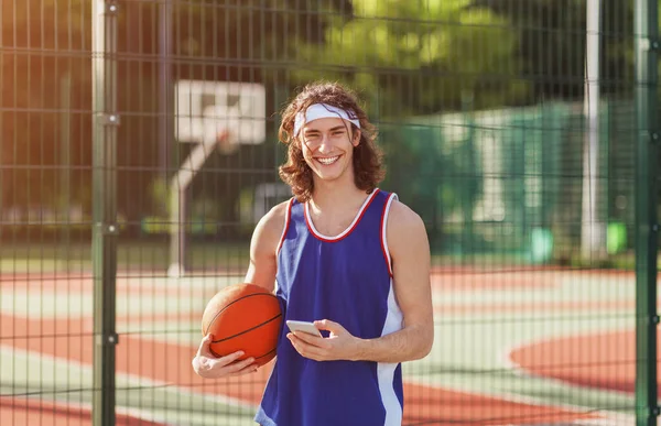 Счастливый миллениал баскетболист с мобильным телефоном на площадке — стоковое фото