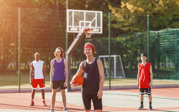 Kaukasia olahragawan memegang bola dengan beragam timnya di arena basket luar ruangan — Stok Foto