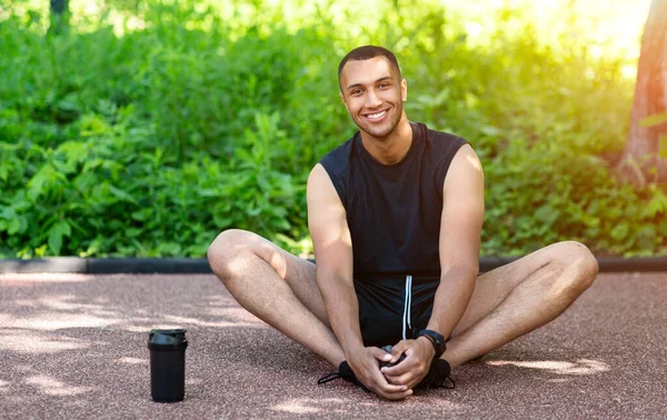 Happy millennial guy doet flexibiliteitsoefeningen na het joggen in het park, lege ruimte — Stockfoto