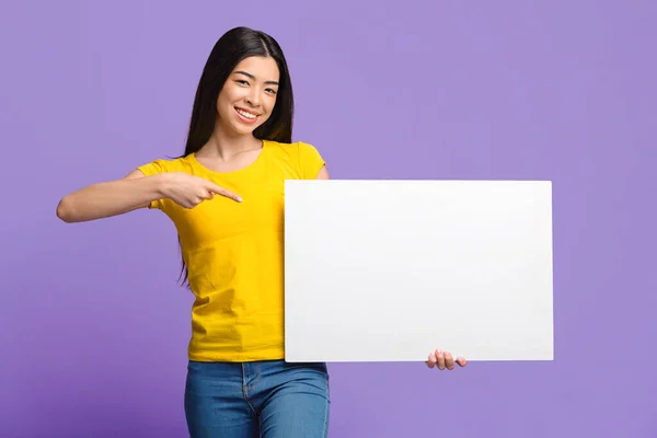 Platz für Ihre Anzeige. Lächelnde asiatische Mädchen zeigen auf weißes Blanko-Plakat — Stockfoto