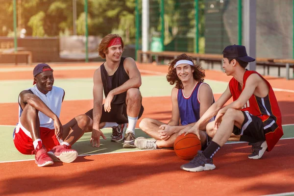 Joyful diverso equipo de baloncesto tomando descanso después de su entrenamiento en la cancha al aire libre — Foto de Stock