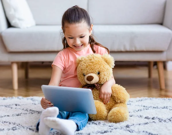 Girl using Digital Tablet néz rajzfilmek Teddy Bear beltéri — Stock Fotó