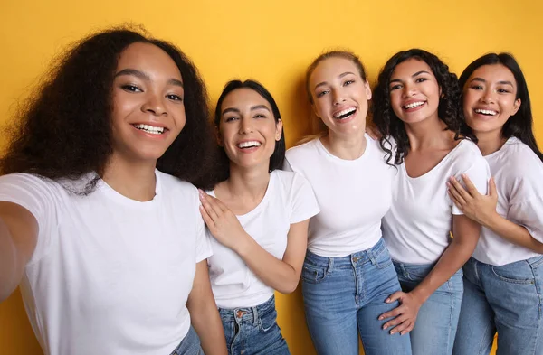 П'ять багаторасові дівчата роблять Селфі позує стоячи над жовтим тлом — стокове фото