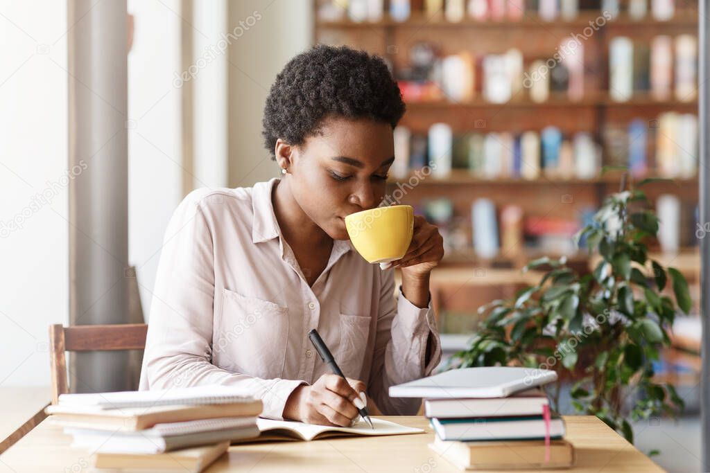 Hardworking female student with heap of books drinking coffee while studying at cafe