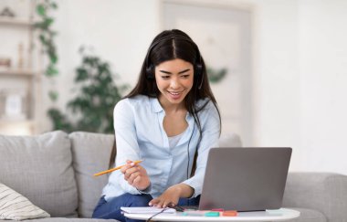 Çevrimiçi Eğitim. Kulaklıklı genç Asyalı kız evde dizüstü bilgisayarla ders çalışıyor.