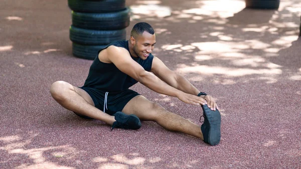 Όμορφος μαύρος με αθλητικά που τεντώνει τους μύες των ποδιών του μετά το τζόκινγκ στο πάρκο. — Φωτογραφία Αρχείου