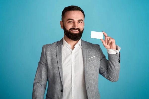 Portrait of cheerful entrepreneur showing business card with empty space for design against blue background — Stok Foto