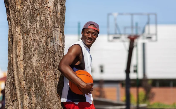 Pemain basket hitam memegang bola dekat arena olahraga luar, ruang kosong — Stok Foto