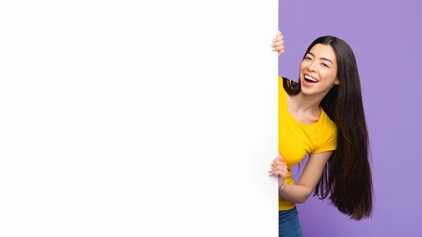 Χαρούμενη Ασιάτισσα κοπέλα που κοιτάζει έξω από το λευκό πίνακα διαφήμισης με ελεύθερο χώρο — Φωτογραφία Αρχείου