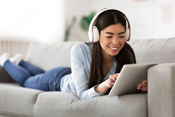 Αγαπημένο Leisure. Ασιατική κορίτσι χαλαρώνοντας με ψηφιακή ταμπλέτα και ακουστικά στον καναπέ — Φωτογραφία Αρχείου