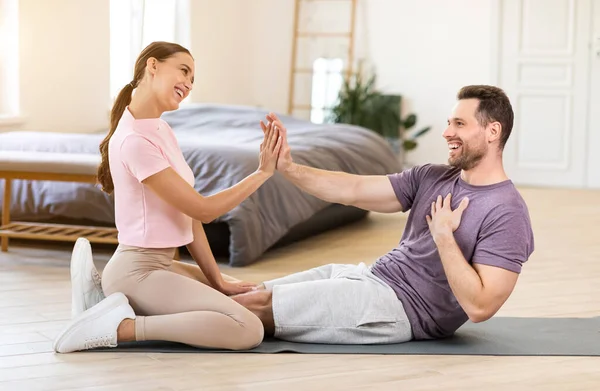 Pareja entrenamiento juntos haciendo abdominales y dando alta cinco en interiores —  Fotos de Stock