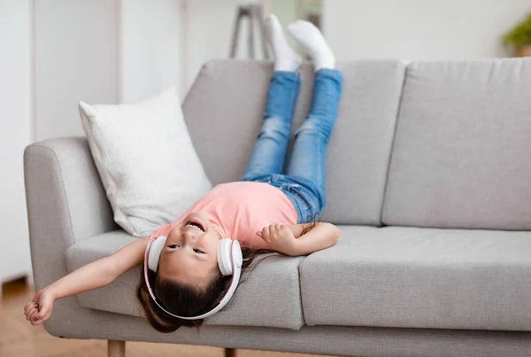 Girl Listening Music Having Fun Sitting Upside-Down On Sofa Indoors — Stok Foto