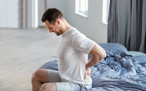 Man masseren terug zittend in bed thuis — Stockfoto