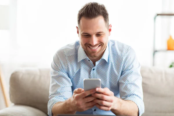 Homem adulto alegre usando telefone inteligente em casa — Fotografia de Stock