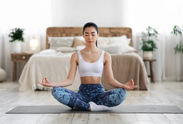 Asiatisk kvinna mediterar hemma, sitter i Lotus position i vardagsrummet — Stockfoto