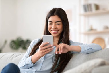Hafta sonu eğlencesi. Gülümseyen Asyalı kız akıllı telefonuyla internette geziniyor.