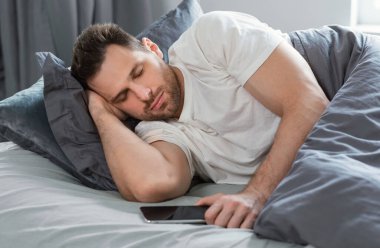 Adam cep telefonunu tutuyor. Evde yatağında yatıyor.