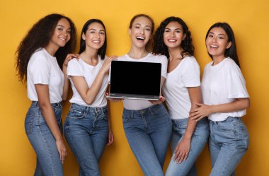 Stüdyonun sarı arka planında dizüstü bilgisayarı olan beş kadın.