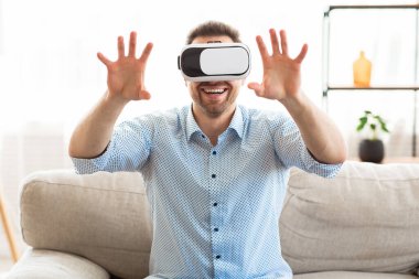 Sanal gerçeklik gözlüğü takan genç adam, kanepede oturuyor.