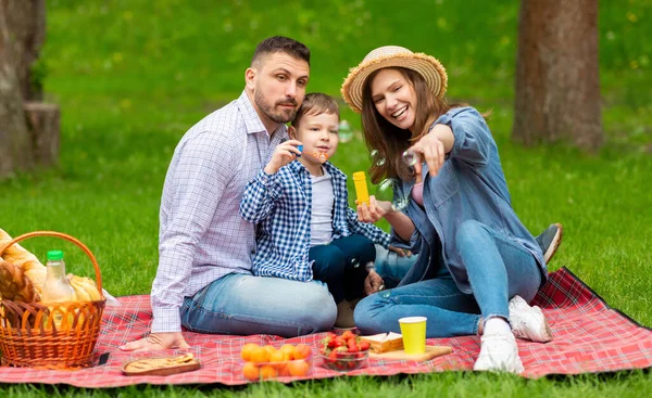 Piknik ailesi eğlencesi. Annesi ve babasıyla kırsal kesimde yaz günü sabun köpüğü üfleyen sevimli bir çocuk. — Stok fotoğraf