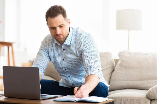 Hombre enfocado usando portátil en casa y escribiendo notas — Foto de Stock