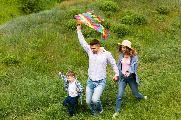 Dreiköpfige Familie läuft mit hellem Drachen in der Hand durch Feld — Stockfoto