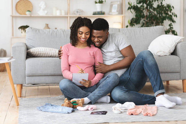 Красивая беременная семья готовит детскую одежду и составляет список
