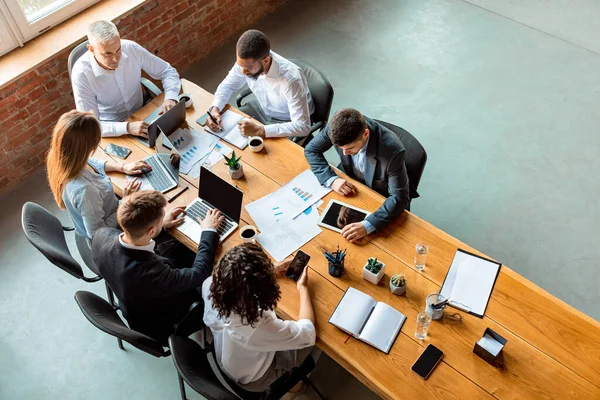 Gruppo di lavoro multirazziale di affari che lavora sedendosi alla tavola in ufficio, alto angolo — Foto Stock