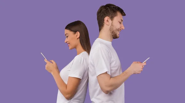 Retrato de pareja joven de pie espalda con espalda usando el teléfono — Foto de Stock