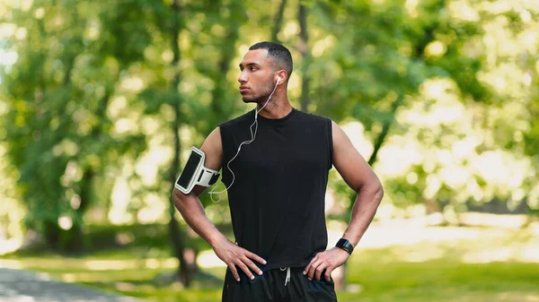 Bonito atleta afro-americano com fones de ouvido ouvindo música durante sua pausa no parque — Fotografia de Stock