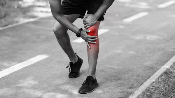 Primer plano del joven deportista sintiendo dolor de rodilla en pista de jogging, efecto blanco y negro —  Fotos de Stock