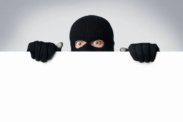 Masked thief peeking out white blank board — Stock Photo, Image