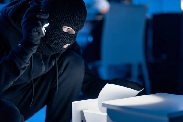 Maskierter Dieb hält vertrauliche Dokumente in Händen und liest — Stockfoto