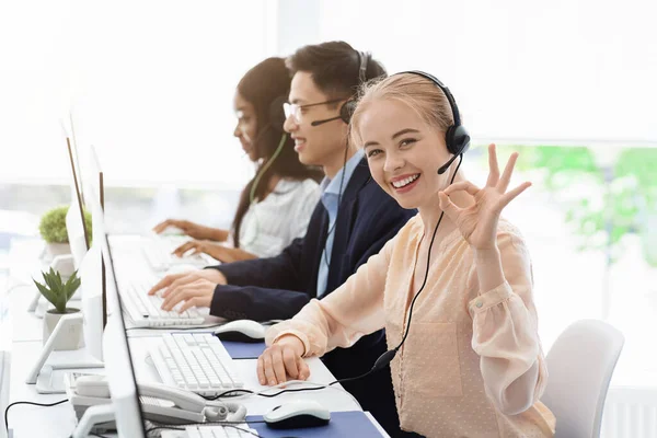 Executivo de atendimento ao cliente mostrando gesto ok e seus colegas que trabalham no call center — Fotografia de Stock