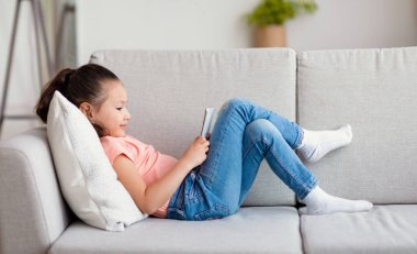 Evdeki koltukta uzanan telefonu kullanan kız.