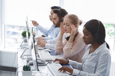 Baş ağrısı çeken teknik destek operatörü ve ofiste bilgisayarlarla çalışan iş arkadaşları.