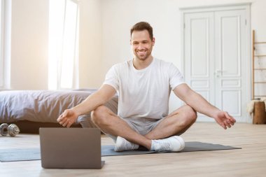 Evde Yoga yapan adam Lotus pozisyonunda oturuyor.