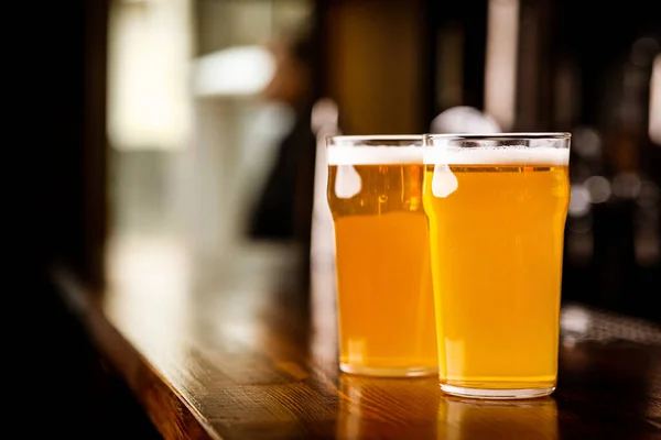 Reunión nocturna en el pub. Dos vasos con cerveza ligera en barra de madera — Foto de Stock