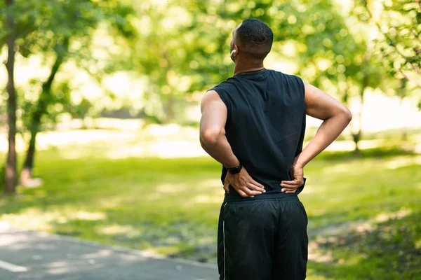 Millennial-Typ in Sportkleidung leidet unter Rückenschmerzen beim Joggen im Park, leerer Raum — Stockfoto