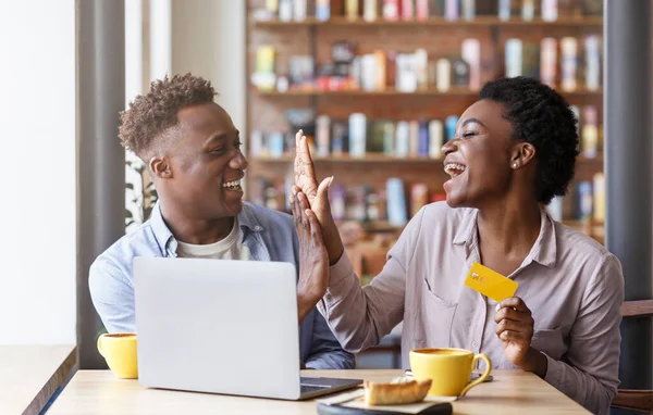 Compras online. Millennial casal preto com cartão de crédito fazendo alto cinco gesto perto laptop no café — Fotografia de Stock