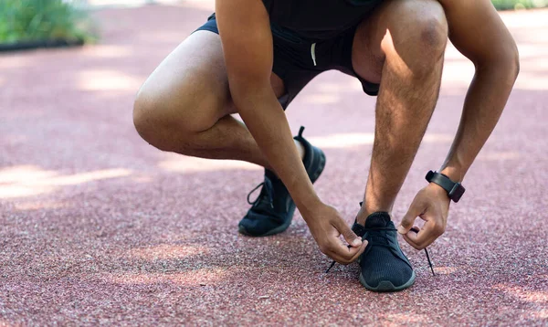 Detailní pohled na černého běžce vázání tkaničky na jeho sportovní obuv během jeho tréninku venku — Stock fotografie